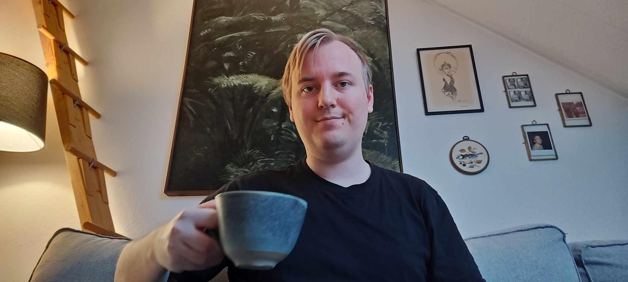 Rasmus Wallberg med en kopp kaffe höjt mot kameran.